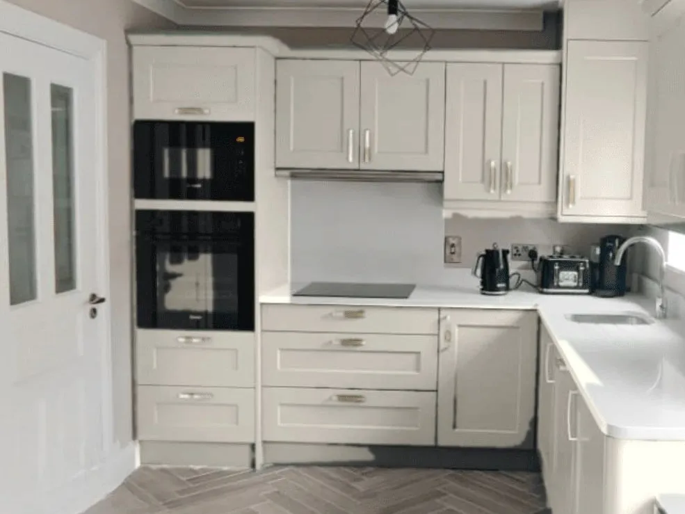 A light shaker-style kitchen with cream doors, a white worktop and built-in ovens