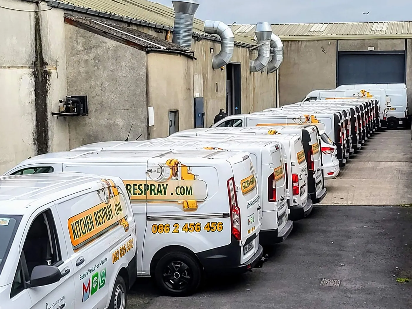 A long line of white Kitchen Respray branded vans parked outside our workshop